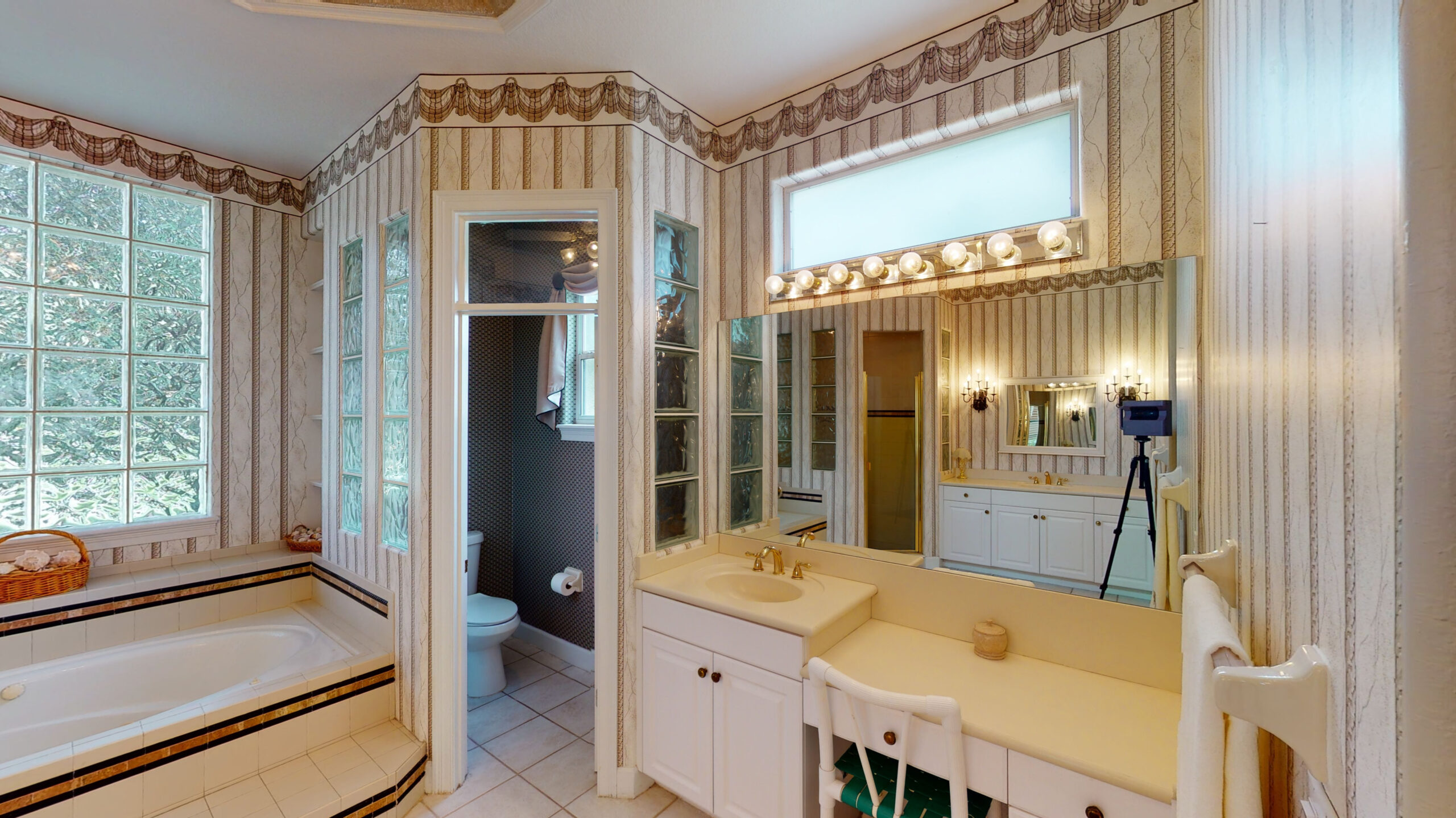 A white bathroom with a wide mirror, table, and chair